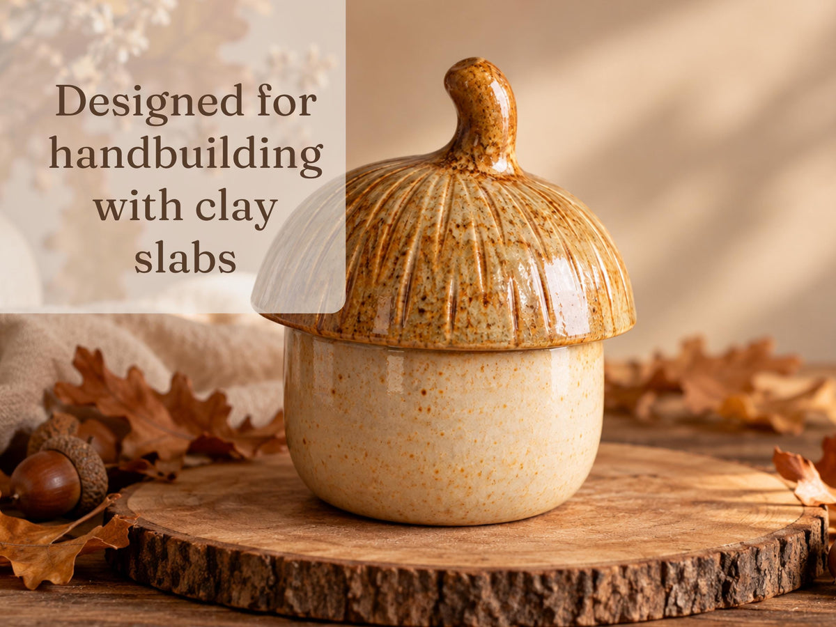 A ceramic acorn-shaped container with a textured surface sits on a wooden surface, surrounded by fallen autumn leaves.