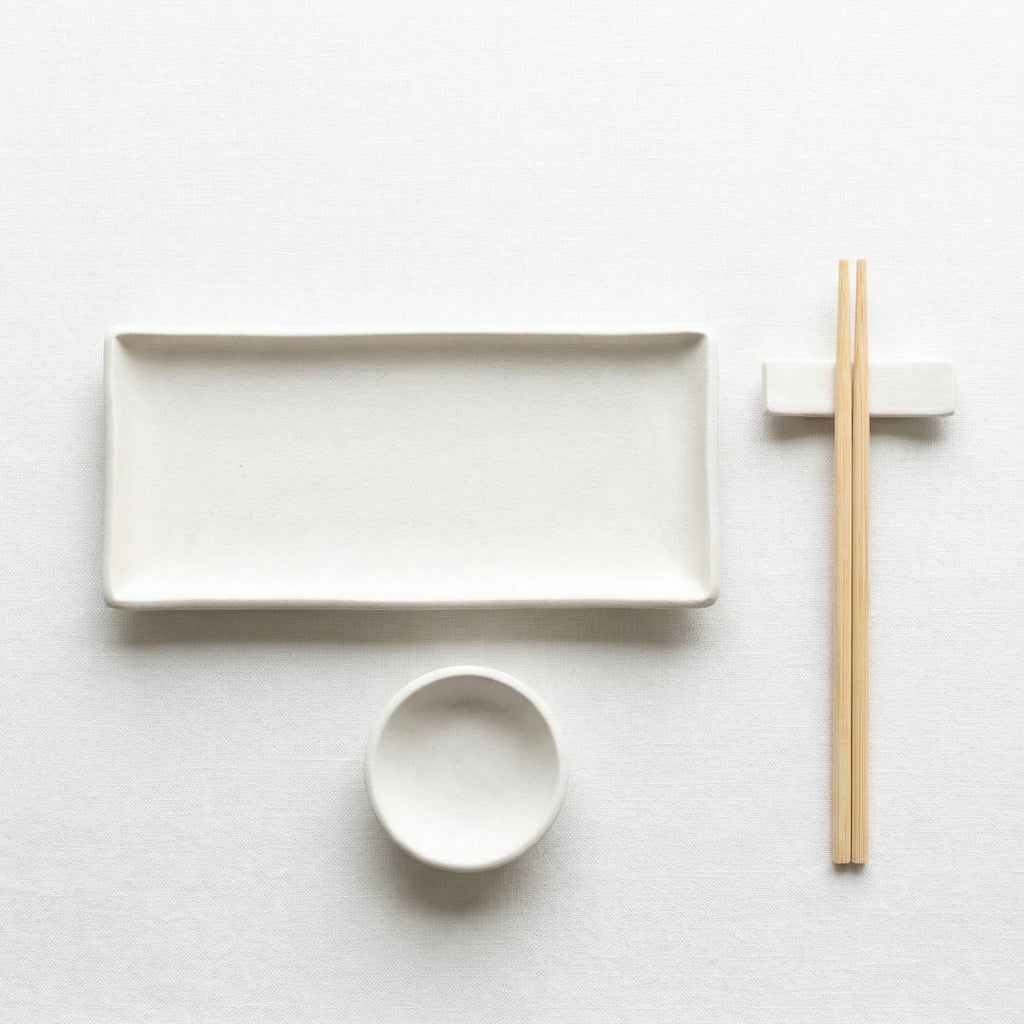a minimalist arrangement of white dishes and chopsticks on a white background.