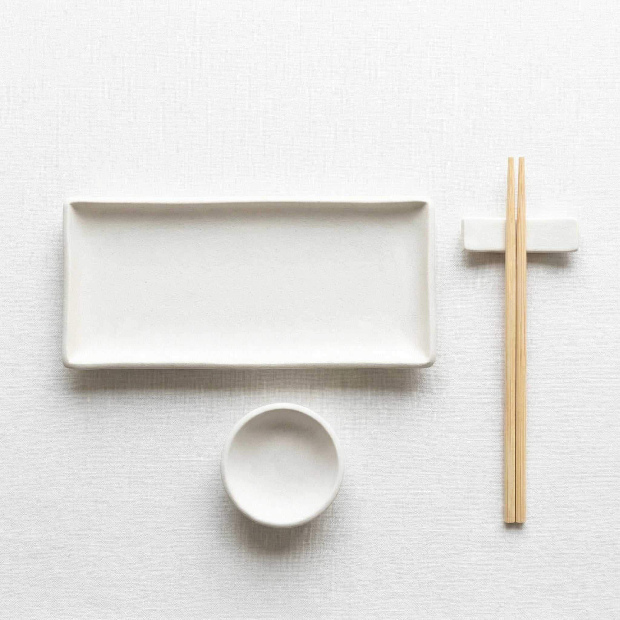a minimalist arrangement of white dishes and chopsticks on a white background.