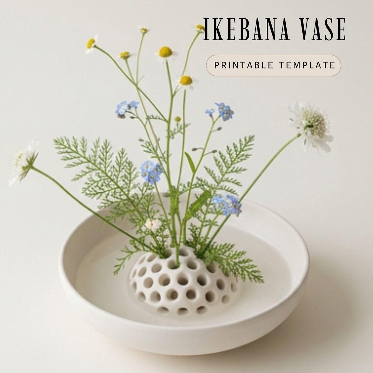 A white Ikebana vase filled with a variety of flowers and foliage, including daisies and ferns, placed in a bowl.