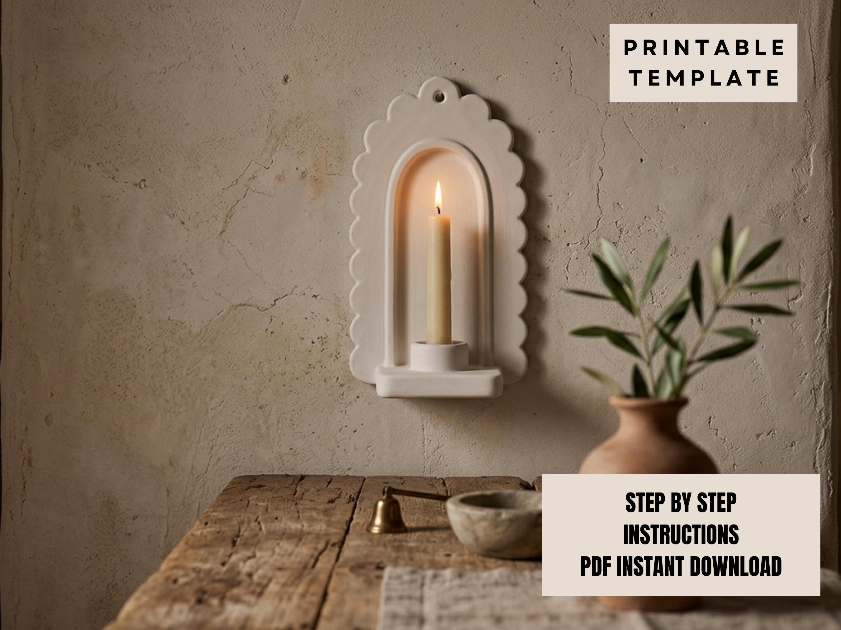 a white candle holder with a lit candle inside, placed on a wooden table. There is also a potted plant and a small bowl on the table. The background is a plain white wall.