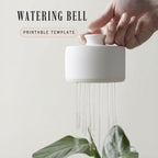 A hand is holding a white ceramic watering bell, which is spraying water onto a plant.