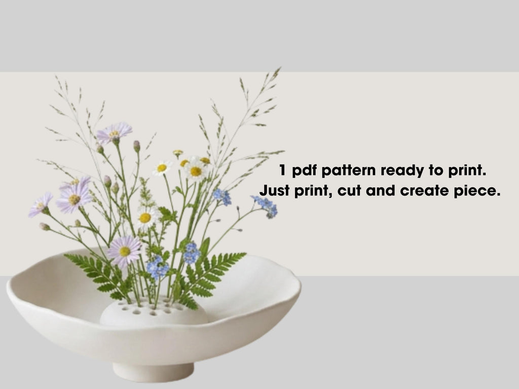 a white vase filled with a variety of colorful flowers, including daisies and blue flowers, placed on a white surface.