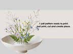 a white vase filled with a variety of colorful flowers, including daisies and blue flowers, placed on a white surface.