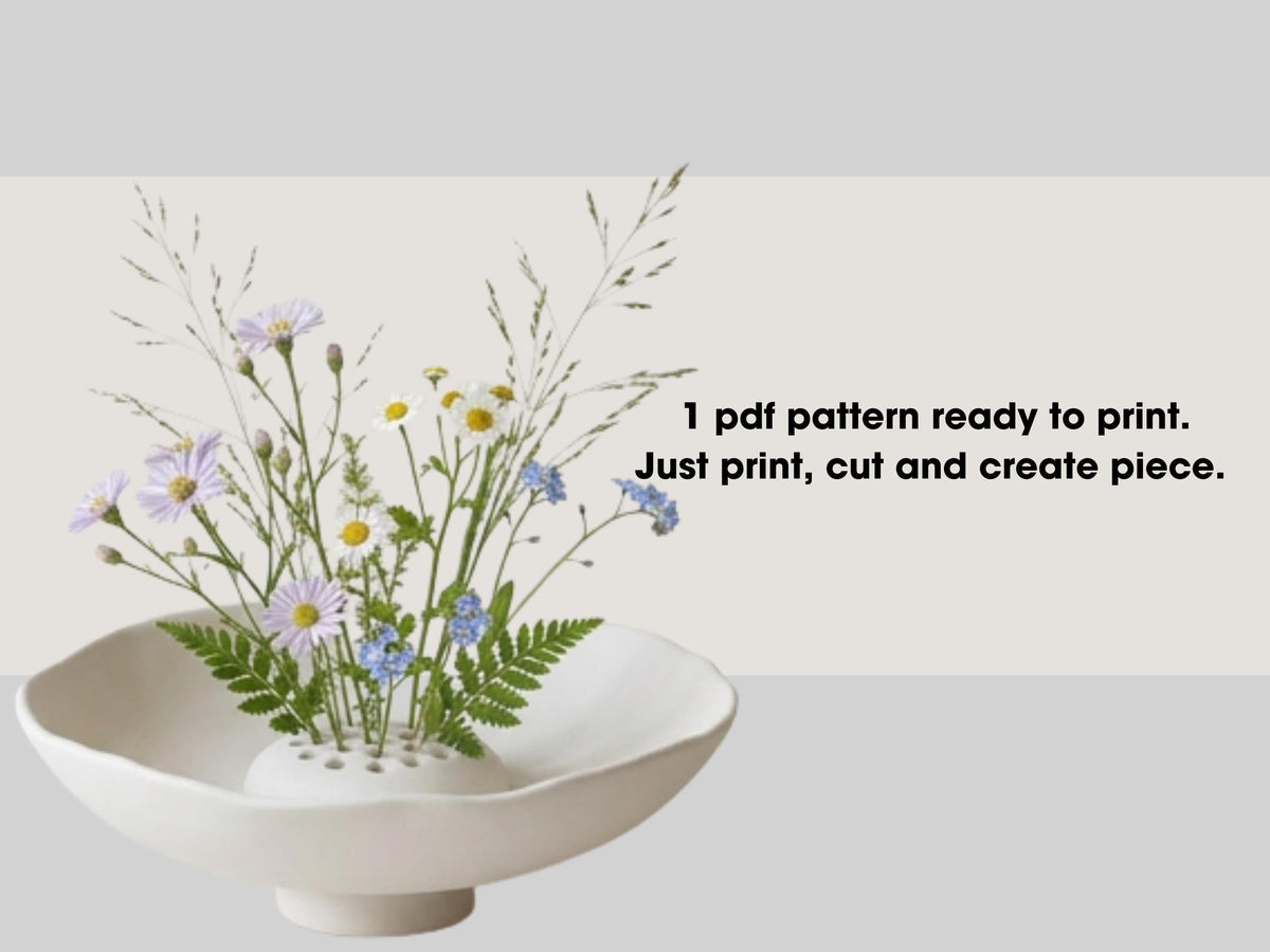 a white vase filled with a variety of colorful flowers, including daisies and blue flowers, placed on a white surface.