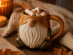 A ceramic mug with a gnome-like design, filled with hot chocolate and marshmallows, sits on a wooden surface next to a book and a candle.