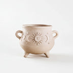 A beige ceramic pot with a sun and moon design on it, sitting on a white background.