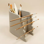 A gray ceramic container holding various paintbrushes and a palette, arranged in a visually appealing manner.