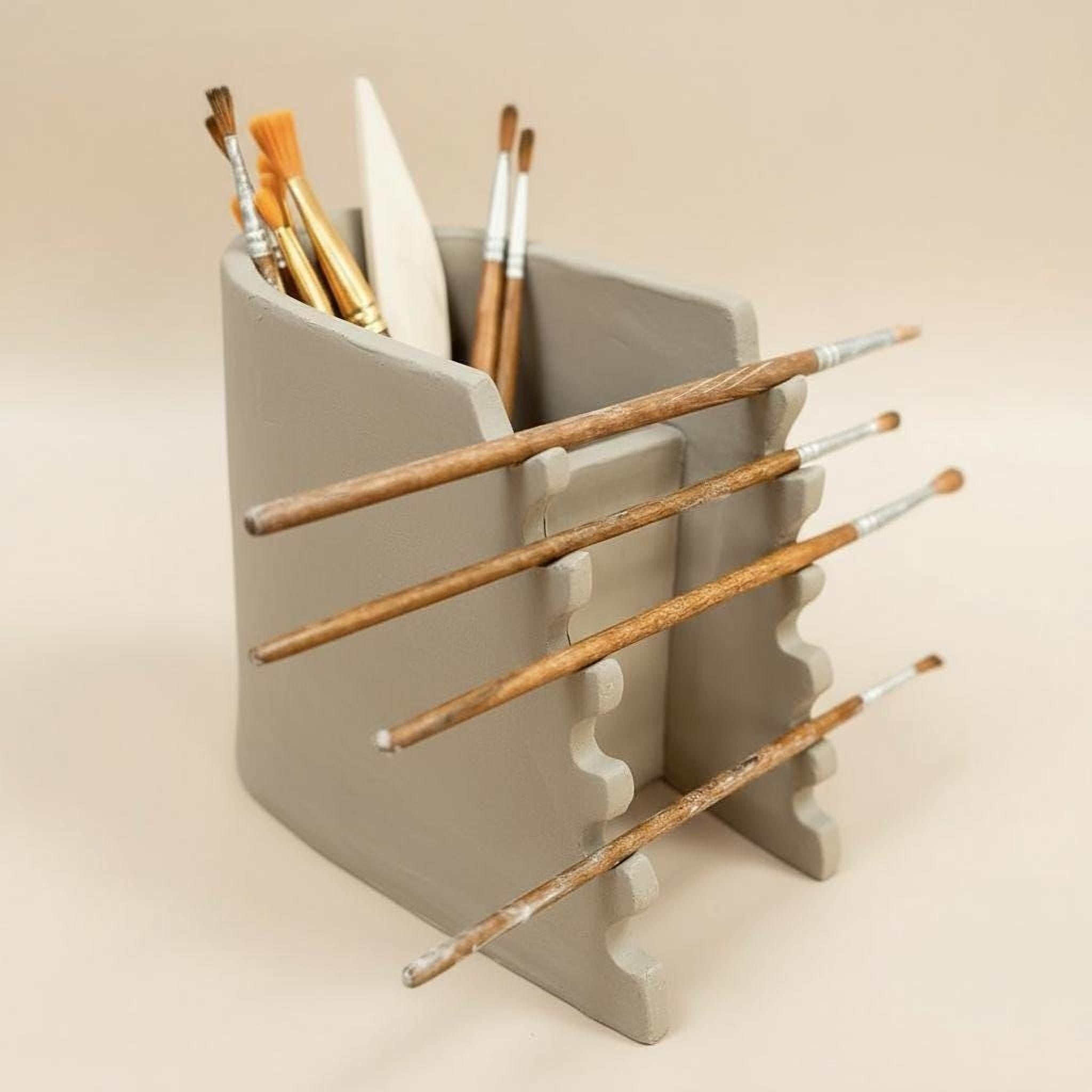 A gray ceramic container holding various paintbrushes and a palette, arranged in a visually appealing manner.