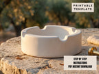 A white ashtray sits on a stone surface, with a blurred natural background.