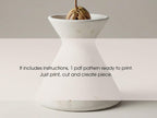 A white ceramic vase with a plant growing in it, accompanied by instructions for creating a similar piece.