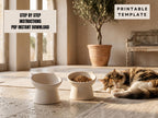 a cat sleeping on a rug in a room with two white bowls, one containing cat food and the other empty. There is a potted plant in the background, and a sign that reads "Step by Step Instructions PDF Instant Download" and "Printable template" is visible.