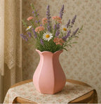 A pink vase filled with a variety of colorful flowers, including daisies and lavender, sits on a wooden table.