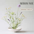 A white Ikebana vase filled with a variety of flowers, including daisies and lavender, against a plain white background.