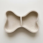 A white ceramic bowl with a unique, organic shape resembling a bone or a bone-like structure.