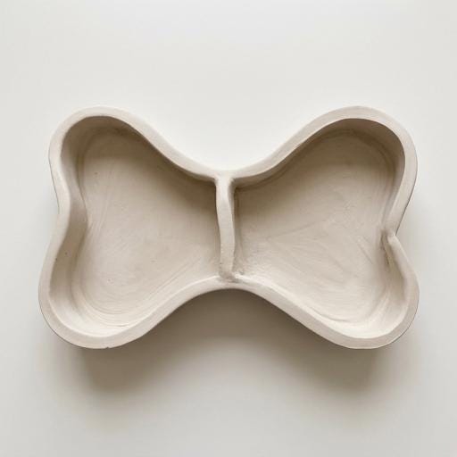A white ceramic bowl with a unique, organic shape resembling a bone or a bone-like structure.