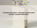A white vase filled with purple and white flowers sits on a white surface, accompanied by text providing instructions for creating a piece of art using the provided pattern.