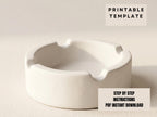 A white ceramic ashtray sits on a plain background.