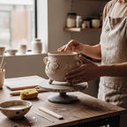 A person is carefully crafting a ceramic pot on a pottery wheel in a pottery studio.