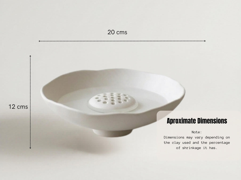 a white ceramic bowl with a hole in the center, placed on a white surface. The bowl appears to be empty, and there is a line indicating the dimensions of the bowl.