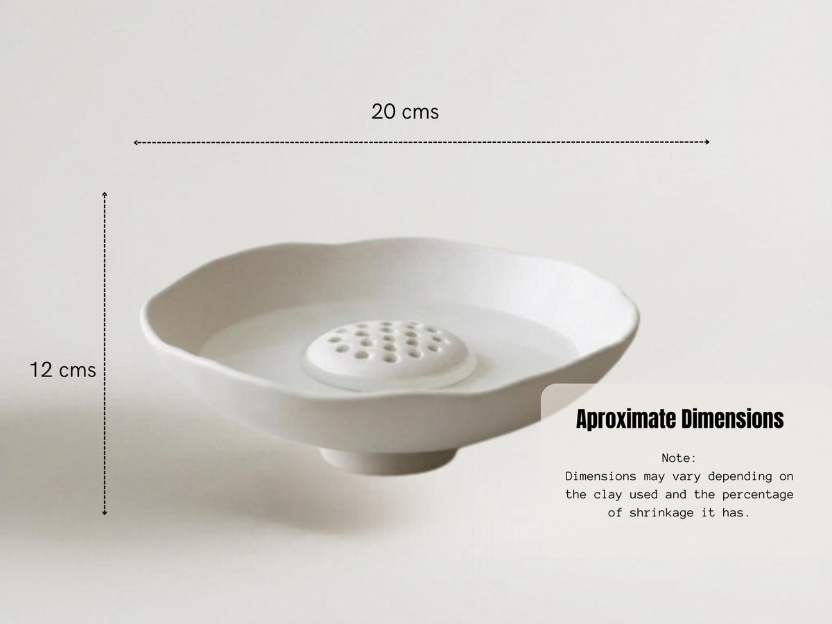 a white ceramic bowl with a hole in the center, placed on a white surface. The bowl appears to be empty, and there is a line indicating the dimensions of the bowl.