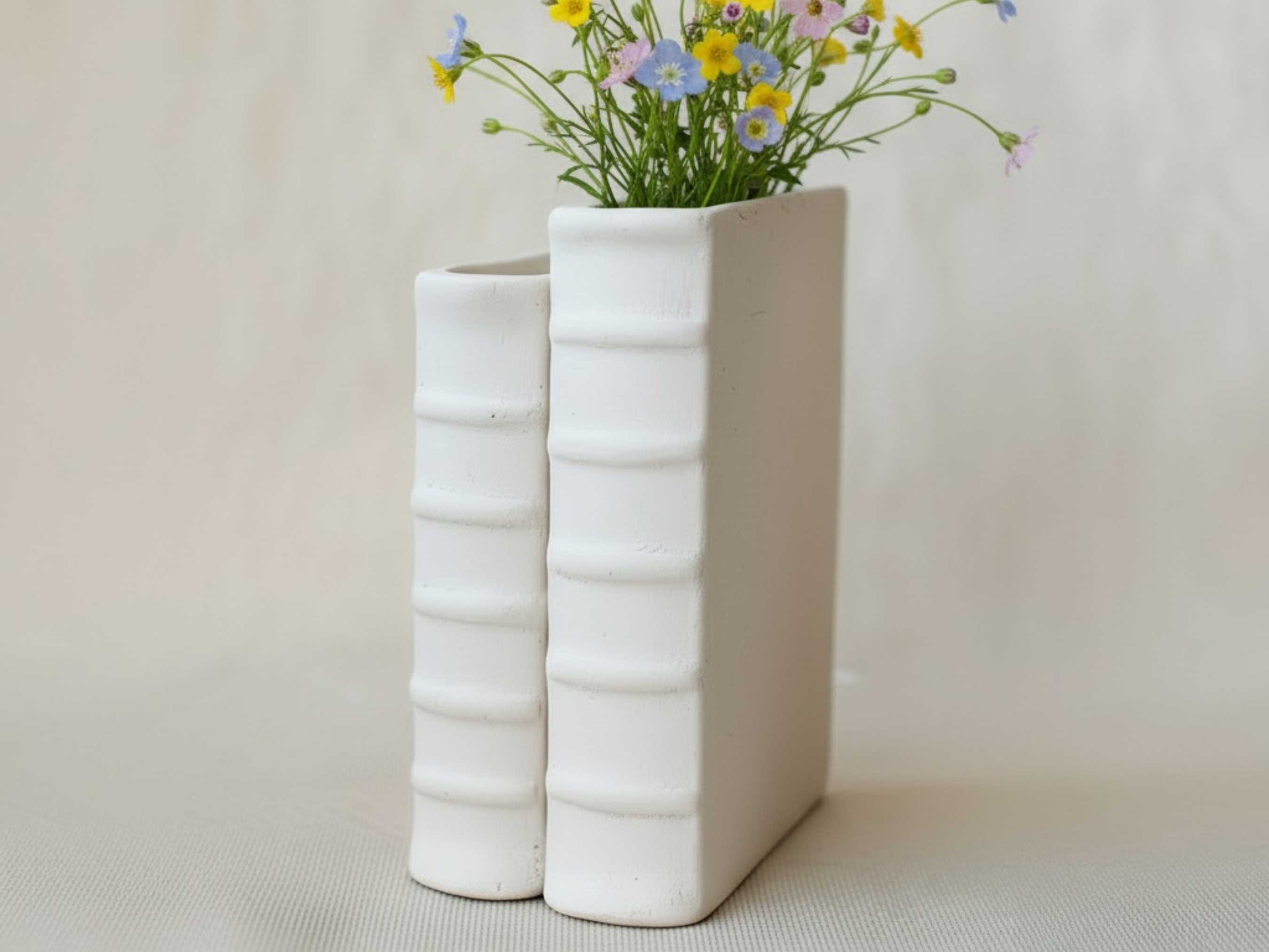A white vase with two vertical book spines, each containing a bouquet of colorful flowers.