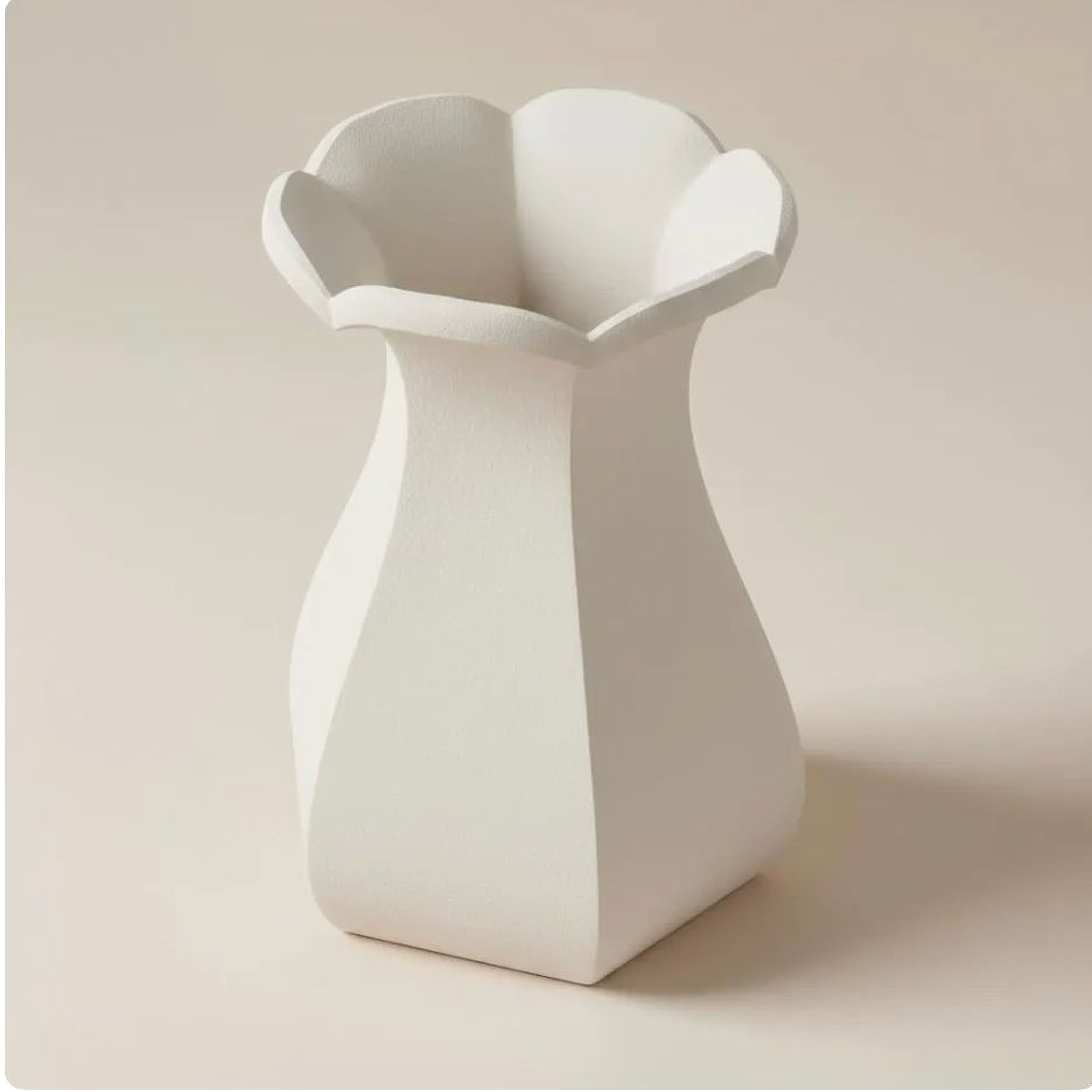 A white ceramic vase with a scalloped edge sits on a plain surface.