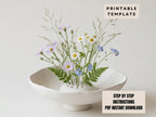 a white ceramic vase filled with a variety of colorful flowers, including daisies and blue flowers, placed on a white surface.