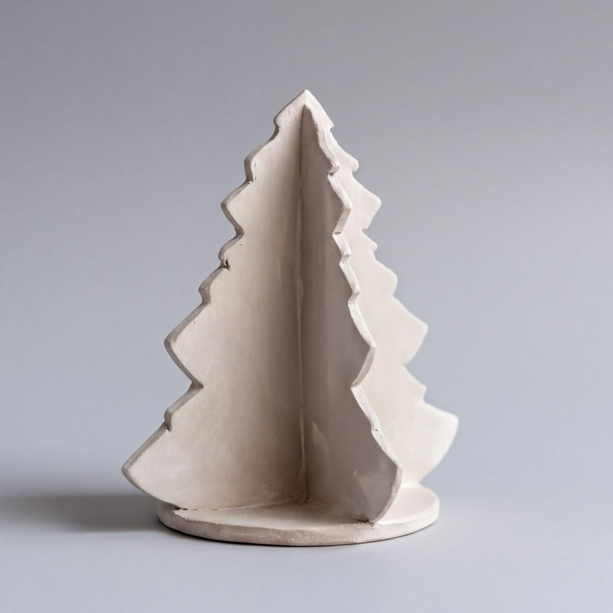 A white ceramic Christmas tree figurine is displayed against a plain gray background.