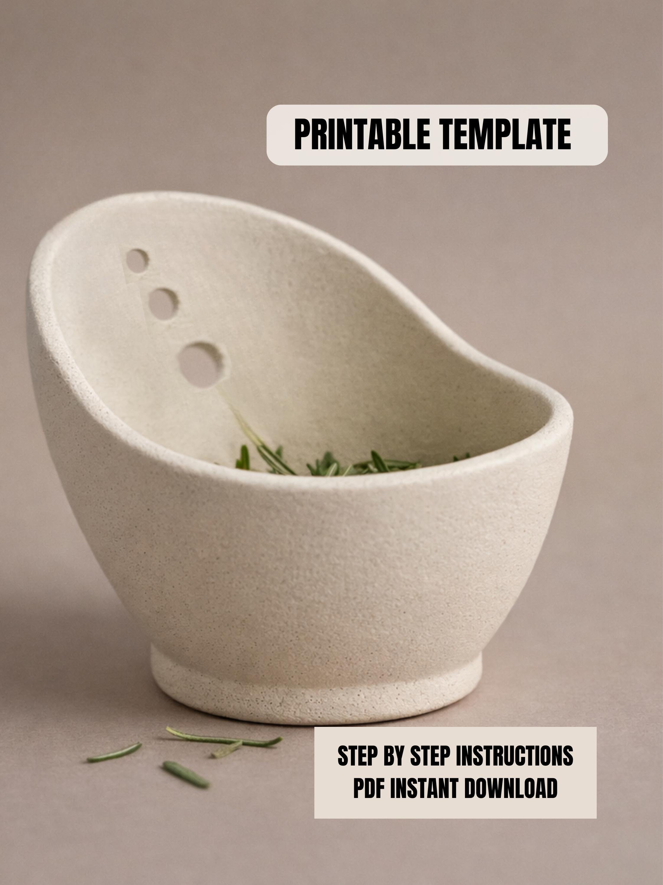 a white ceramic bowl with a few holes in it, placed on a surface with some green leaves scattered around it.